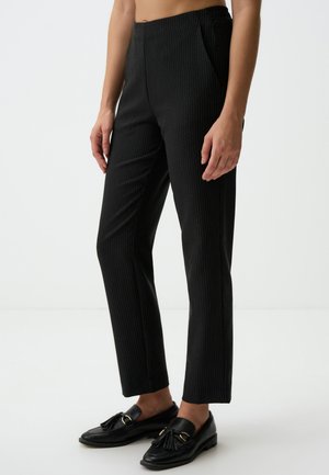 Pantaloni neri con righe sottili e vestibilità su misura, caratterizzati da una parte anteriore piatta, tasche laterali e una texture liscia. Indossati con mocassini neri.