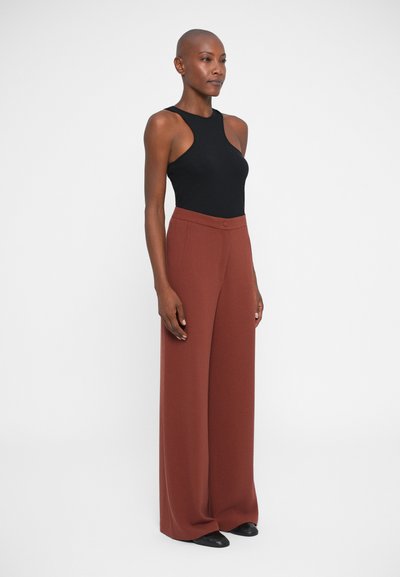 Top negro sin mangas con diseño recortado, combinado con pantalones de pierna ancha en color óxido que cuentan con un botón frontal y una textura suave.