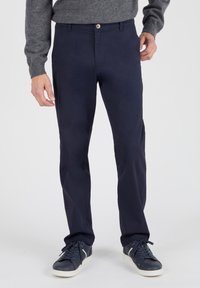Marineblauwe chinos van katoen met een gladde textuur, voorzien van een frontknop, ritssluiting en zijzakken. Gecombineerd met donkere sneakers.