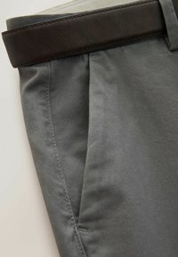 Zbliżenie na szare spodnie z boczną kieszenią i wplecionym przez szlufkę ciemnobrązowym skórzanym paskiem.