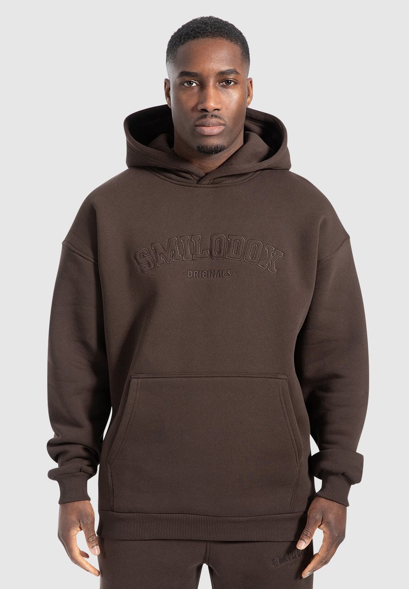 Brun hoodies med framficka, oversized passform, ribbade ärmslut och nederkant, med präglad logotyp "SMILODOX ORIGINALS". Mjuk textur.