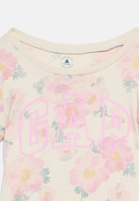 Παιδικό πουκάμισο Baby Gap με λουλουδάτο σχέδιο και ροζ γράμματα GAP στο μπροστινό μέρος, με στρογγυλή λαιμόκοψη.