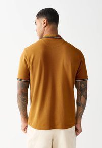 Krátky rukáv polokošeľa v horčicovej žltej farbe s čierno-bielym pruhovaným golierom. Jemná, textúrovaná látka so strihom na rovno bez viditeľných log.