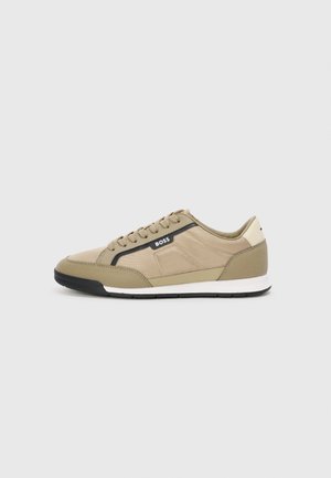Tan sneaker with a textured fabric upper, black accents, and a white sole. Features a lace-up design and logo on the side.