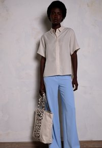 Light beige short-sleeve shirt, blue wide-leg trousers, and a tote bag with a leopard print accent. Smooth fabric and relaxed design.