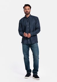 Donkerblauwe overhemden met een zak, gecombineerd met lichtblauwe denim jeans en zwarte instap schoenen. Eenvoudig, casual ontwerp.