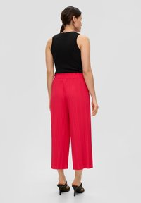 Zwarte mouwloze top gecombineerd met hooggetailleerde, geplooide, felroze culottes, enkel-lang, met een wijd beenontwerp en elastische tailleband.