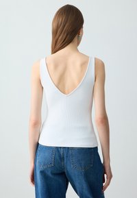 Canottiera bianca a costine con design a V sul retro, abbinata a jeans in denim blu a vita alta, con tasche cucite e una vestibilità leggermente loose.