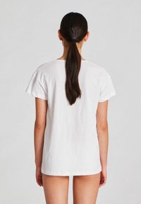 Tricou alb din bumbac, cu mâneci scurte, croi lejer, decolteu rotund și o textură netedă. Vederea din spate arată un design simplu, neîmpodobit.