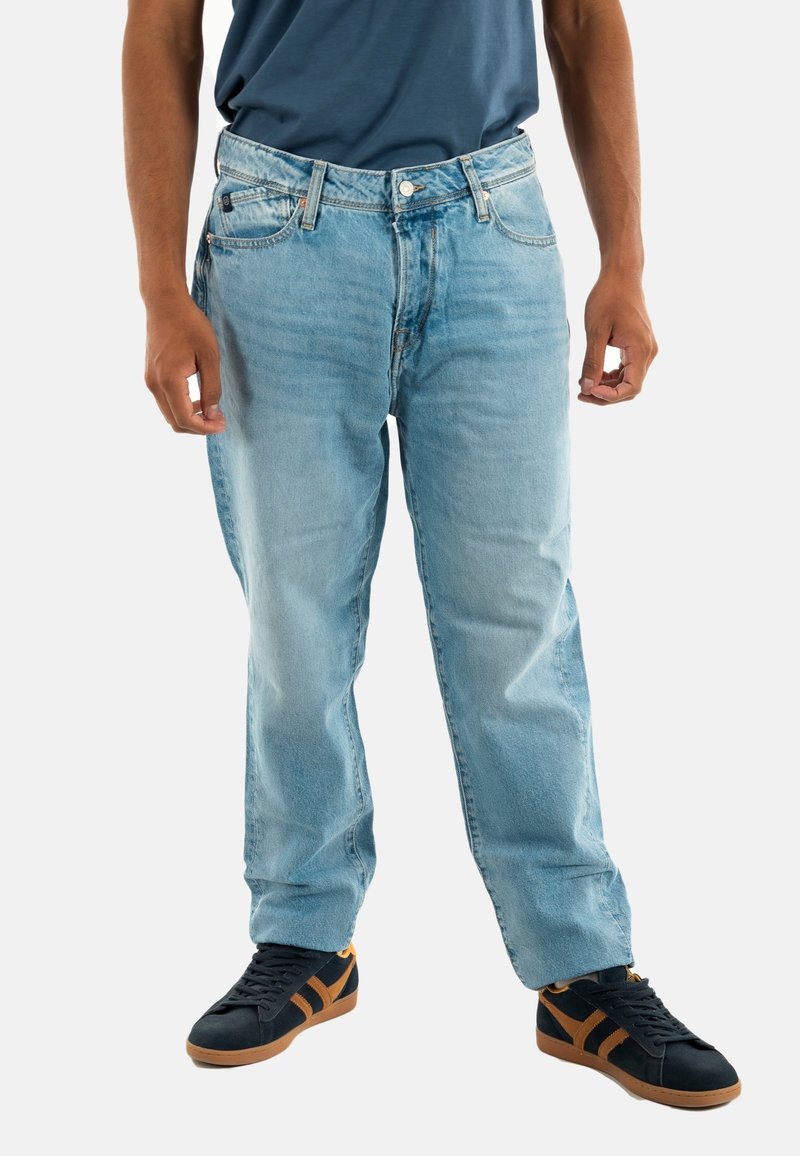 Pantalones vaqueros de mezclilla azul claro con un diseño recto, estilo de cinco bolsillos y un acabado desgastado. Llevados con zapatillas negras con detalles en marrón.