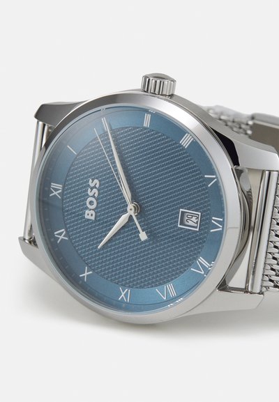 Montre avec un bracelet en maille argentée, un cadran texturé bleu, des chiffres romains et une fenêtre de date. Dispose d'un boîtier en acier inoxydable poli et d'une couronne.