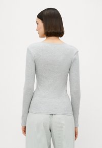 Haut à manches longues gris avec un col en U et une silhouette ajustée. La texture est douce. Modèle associé à un pantalon rayé, vue de dos.