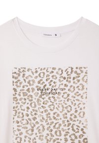 T-shirt bianco a maniche corte, caratterizzato da una stampa leopardata dorata e dal testo "OGNI GIORNO È IL TUO GIORNO" centrato all'interno del design.