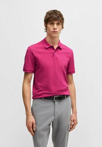 Fitted kortärmad polotröja i en livlig rosa bomull, med klassisk krage och broderad logotyp, kombinerad med ljusgrå byxor.