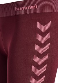 Nærbillede af burgunder leggings med lyserøde chevron-striber ned langs siden og lyserødt "hummel" logo på taljebåndet.