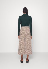 Camisola verde de manga longa combinada com calças largas de cintura alta com um padrão floral em rosa e branco sobre um fundo caqui.