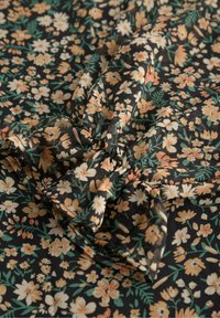 Svart tyg med ett blommönster som har små orange och vita blommor och gröna blad, med en rynkad detalj vid sömmen.