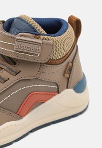 Bruine leren sneaker met mesh details, oranje en blauwe accenten, en een verhoogde hak. Voorzien van een klittenbandsluiting en een logo label.