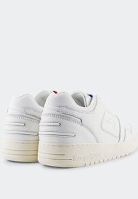 Sneaker bianche in pelle con dettagli testurizzati, suole in gomma e un logo. Presentano accenti rossi e blu sul tallone.