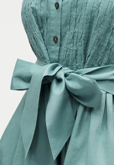 Φόρεμα ανοιχτό τιρκουάζ με υφή στο μπούστο, καφέ κουμπιά και φαρδιά υφασμάτινη ζώνη δεμένη σε φιόγκο στη μέση.