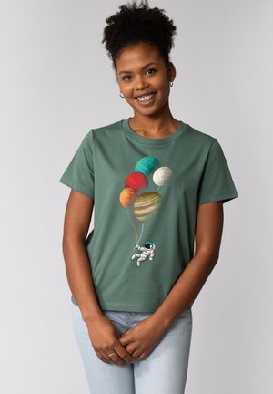 Groene katoenen T-shirt met een astronaut die kleurrijke planetenvormige ballonnen vasthoudt, weergegeven tegen een neutrale achtergrond.