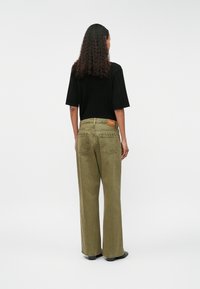 Zöld, bő szárú nadrág, texturált felülettel, hátsó derékra varrt címkével és letisztult, igényes megjelenéssel. Fekete, rövid ujjú blúz.