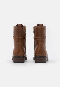 Braune Leder-Stiefeletten mit Reißverschluss, dekorativen Riemen und niedrigem Blockabsatz. Glatte Textur mit dezenten Nahtdetails.