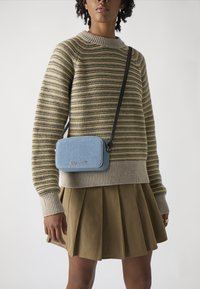 Knitted striped sweater in yellow, gray, and navy. A light blue crossbody bag with silver hardware rests on a tan pleated skirt.