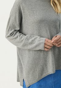 Grå stickad tröja med avslappnad passform och långa ärmar, som har en rundad halsringning och sidofickor; i kombination med en blå kordflamskjol.