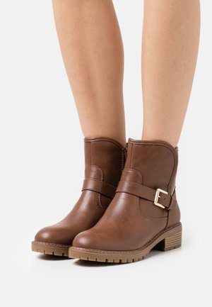 Stivali ankle in pelle marrone con zip laterale, dettaglio fibbia e suola in gomma testurizzata. Parte superiore liscia con dettagli cuciti e tacco basso.