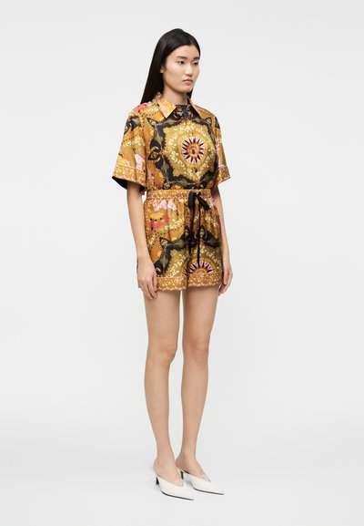 Mono corto de manga corta color marrón con patrones florales y geométricos coloridos, cintura con cinturón y un cuello. Se lleva con zapatos blancos puntiagudos.