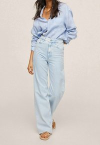 Jeans de tiro alto y pata ancha en azul claro con un lavado deslavado, combinados con una camisa de botones a rayas en azul claro, hecha de una tela suave.