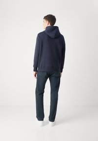 Marineblå hettegenser med snorhette, avslappet passform, lange ermer, sammen med mørke denimjeans og hvite joggesko. Jevnt, strukturert stoff.