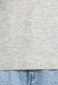 Pull gris clair en tricot avec un détail de bord-côte à l'ourlet, associé à un jean en denim. Le pull présente une finition douce et texturée.