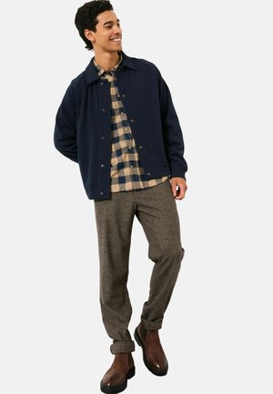 Navy blue jacket over a beige and black plaid shirt, gray textured pants, and brown boots, featuring a casual fit and simple button details.