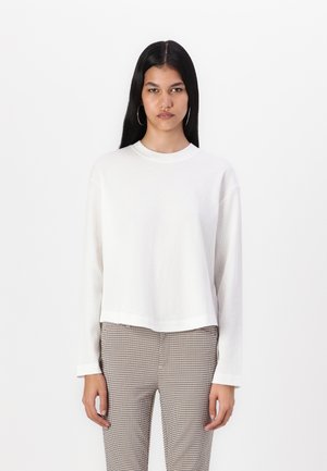 Top bianco a maniche lunghe con texture a coste, scollatura rotonda e orlo corto. Abbinato a pantaloni a quadri grigi e neri.