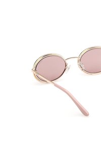 Lunettes de soleil rondes avec monture en métal doré et verres teintés roses, dotées d'embouts de branches roses et de plaquettes nasales réglables.