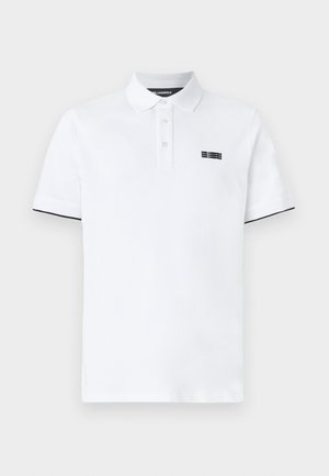 Hvit polo-skjorte laget av bomull, med en svart logo på venstre bryst og svarte detaljer på ermene. Klassisk krage og knappestolpe.