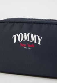 Mørkeblå nylonveske med hvit tekst "TOMMY" og "New York" i rødt, med en glatt tekstur og glidelås-lukking.