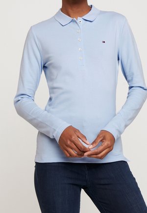 Lyseblå polo med lange ærmer, knapper foran og blød tekstur. Har en lille logo på brystet og en klassisk krave.