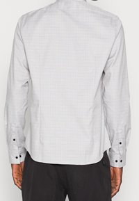Camicia grigia a quadri con maniche lunghe, polsini con bottoni e orlo dritto. Presenta una texture sottile e una vestibilità pulita e su misura.