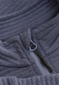 Marinblå zipjacka i fleece med texturerat ribbat tyg, platta sömmar och en distinkt dragflik för enkel öppning.