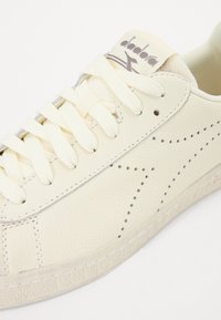 Sneaker in pelle crema con design con lacci, superficie texturizzata, accenti perforati e cuciture a contrasto. Logo sulla linguetta.