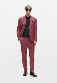 Burgundi színű, slim fit zakó finom textúrával, fekete inggel, fekete övvel, zsebkendővel és sötét napszemüveggel párosítva. Fekete loafer cipők.