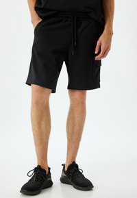 Pantalones cortos deportivos negros con cintura elástica y cordón ajustable. Cuentan con un bolsillo lateral y una tela suave y ligera.