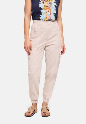 Mujer que lleva pantalones cargo beige con puños elásticos, un top sin mangas azul marino con un gráfico colorido de jirafa y sandalias beige con hebillas.