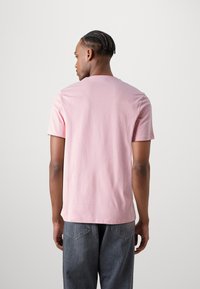 Lys rosa bomulls t-skjorte med rund hals, korte ermer og avslappet passform, kombinert med mørke grå denimbukser. Myk tekstur, minimal design.