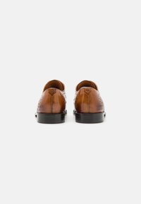 Scarpe in pelle marrone con una finitura liscia, perforazioni decorative e suola in gomma nera. Tacco arrotondato e design minimalista.