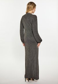 Maxi dress nera con texture, maniche lunghe, design a coste e accenti metallici, caratterizzata da una silhouette aderente e un leggero lucido.