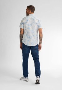 Korte mouwen shirt met een blauw bloemenpatroon op een lichte achtergrond, gecombineerd met donkerblauwe jeans en witte sportschoenen.